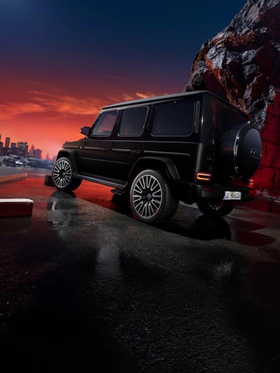 Mercedes-AMG G63 mit Two-Finish Paket in seitlicher Rückansicht auf schwarzer Fläche mit Felsen und Sonnenuntergang im Hintergrund.