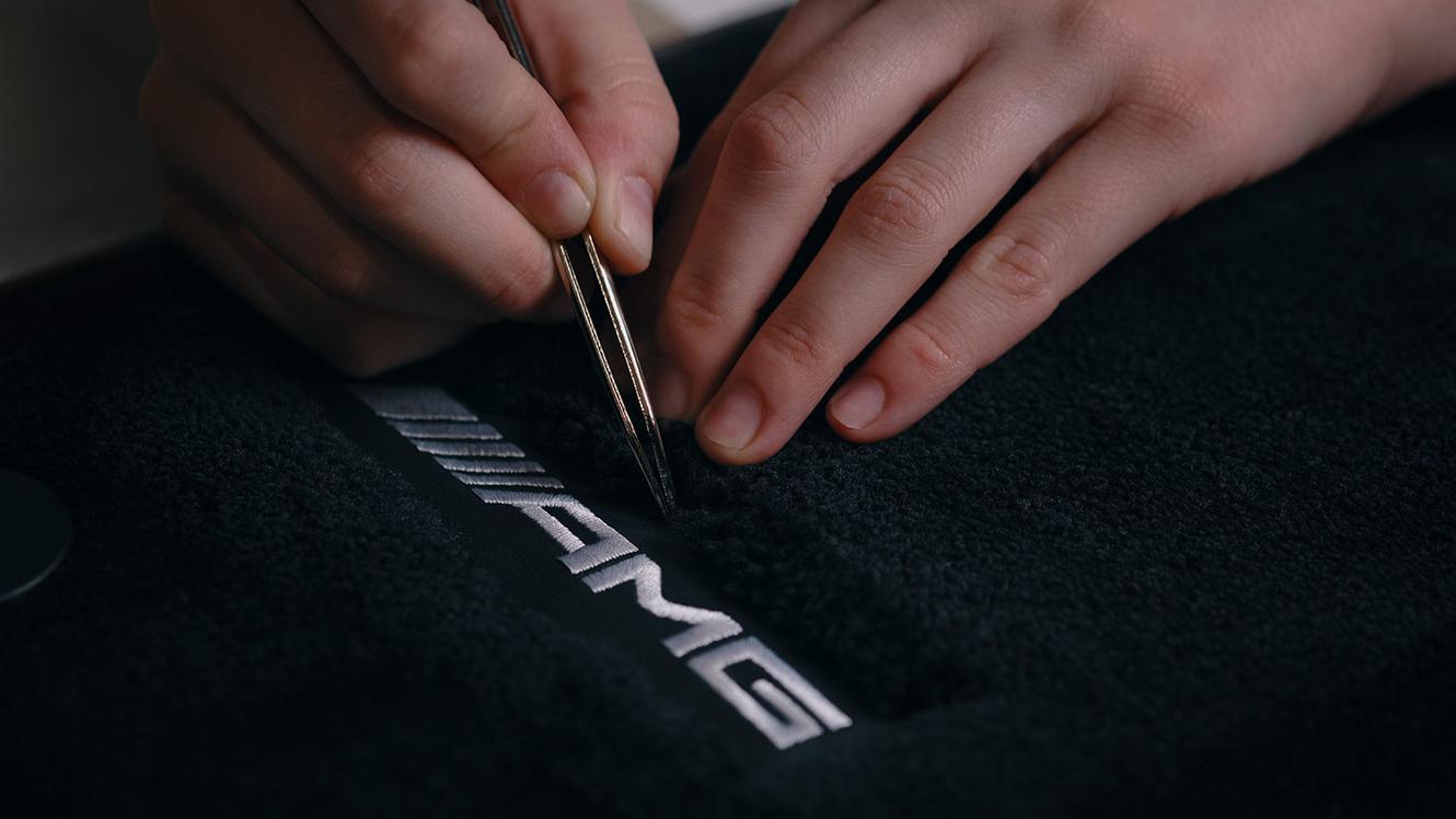 Zwei Hände im Fokus beim Nähen des AMG Schriftzuges.