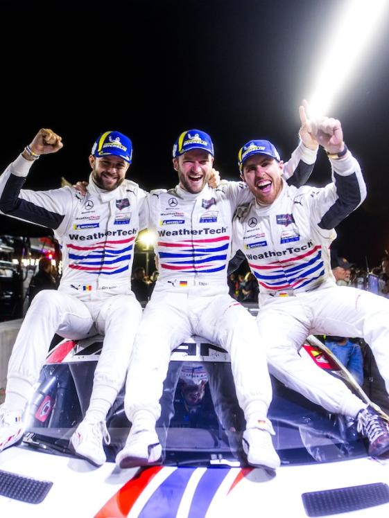 3 cheering AMG GT racing drivers sit on their racing car