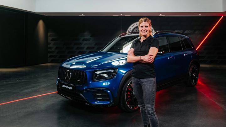 Der blaue Mercedes AMG GLB SUV mit der Produktmanagerin davor.