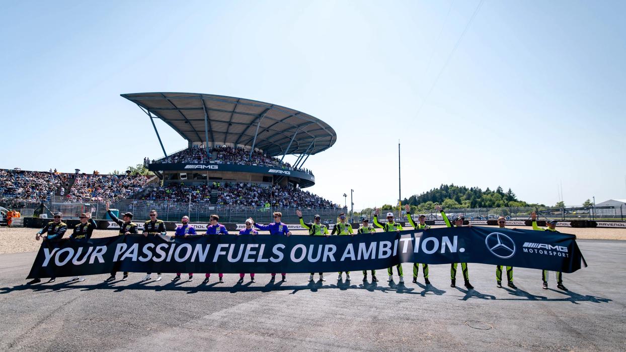 Four Mercedes-AMG GT team members hold a banner with ‘Your passion fuels our ambition’